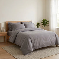 Bedroom with a bed covered in gray bedding and pillows, wooden headboard, and plants.
