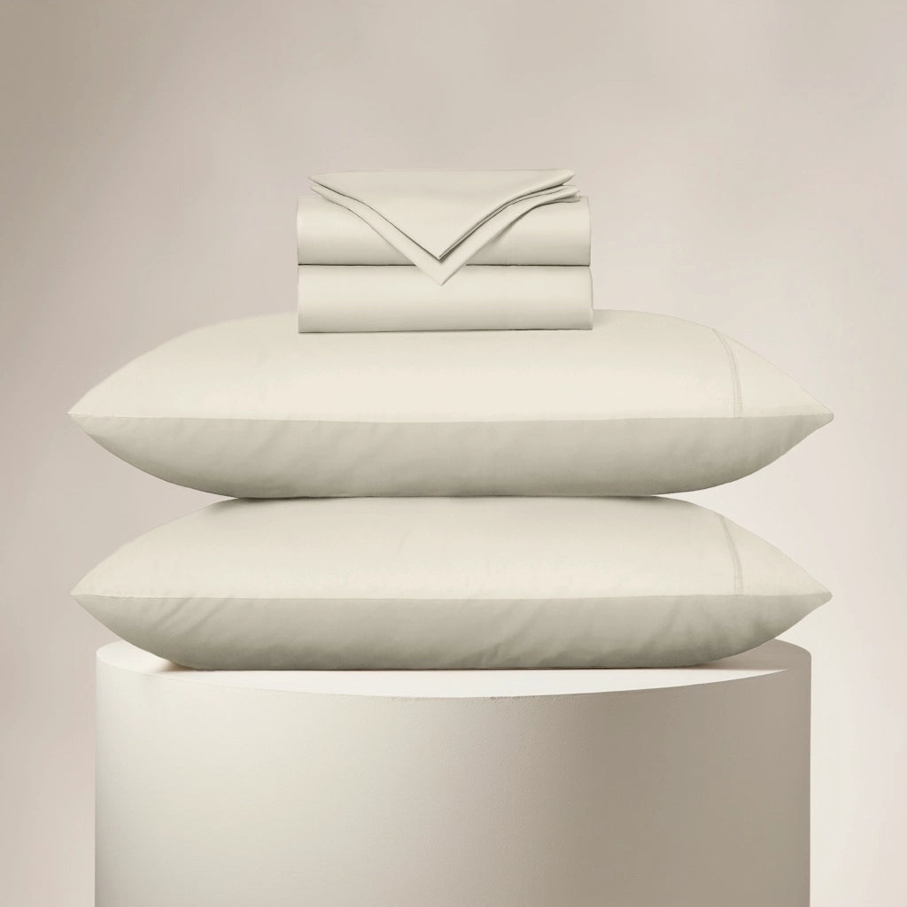Stack of light-colored pillows and a folded sheet on a neutral background
