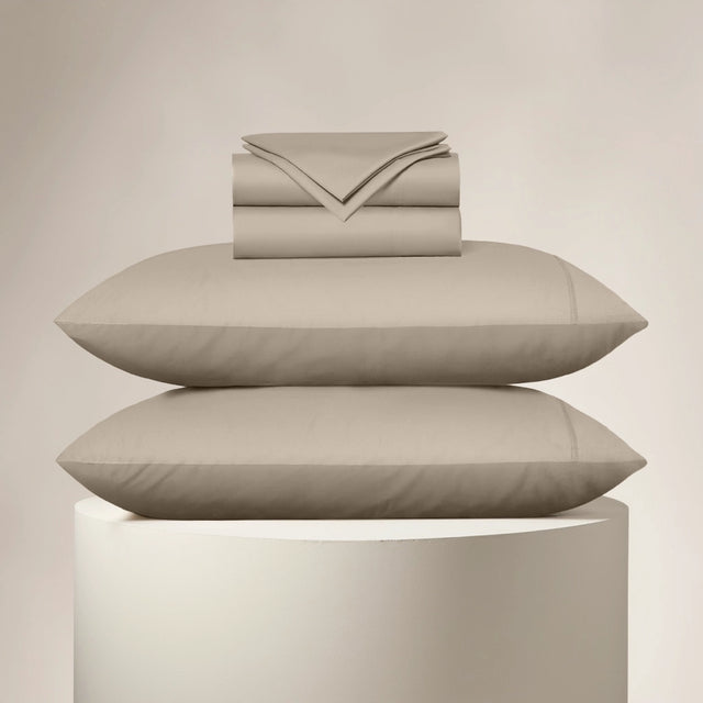 Beige bed sheets and pillows stacked on a beige pedestal against a beige background
