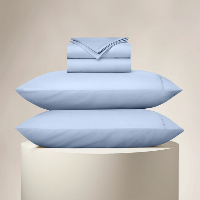 Set of light blue bedding including a duvet, pillowcases, and bed sheets on a beige background.
