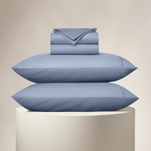 Set of blue bedding including pillows and a folded sheet on a beige background