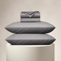 Gray bedding set including a duvet, two pillows, and a folded blanket on a beige background