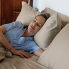 Woman in a blue shirt lying in bed with beige pillows and bedding.