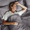 Woman sleeping under gray bedding in a bed