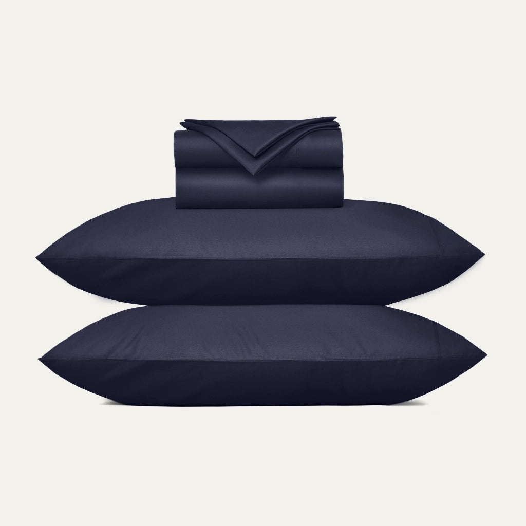Navy blue bedding set including duvet, two pillows, and a folded blanket on a light gray background