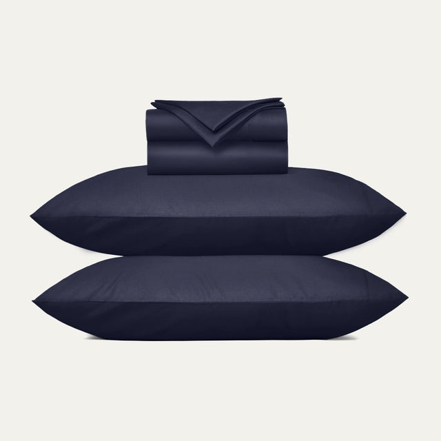 Navy blue bedding set including duvet, two pillows, and a folded blanket on a light gray background