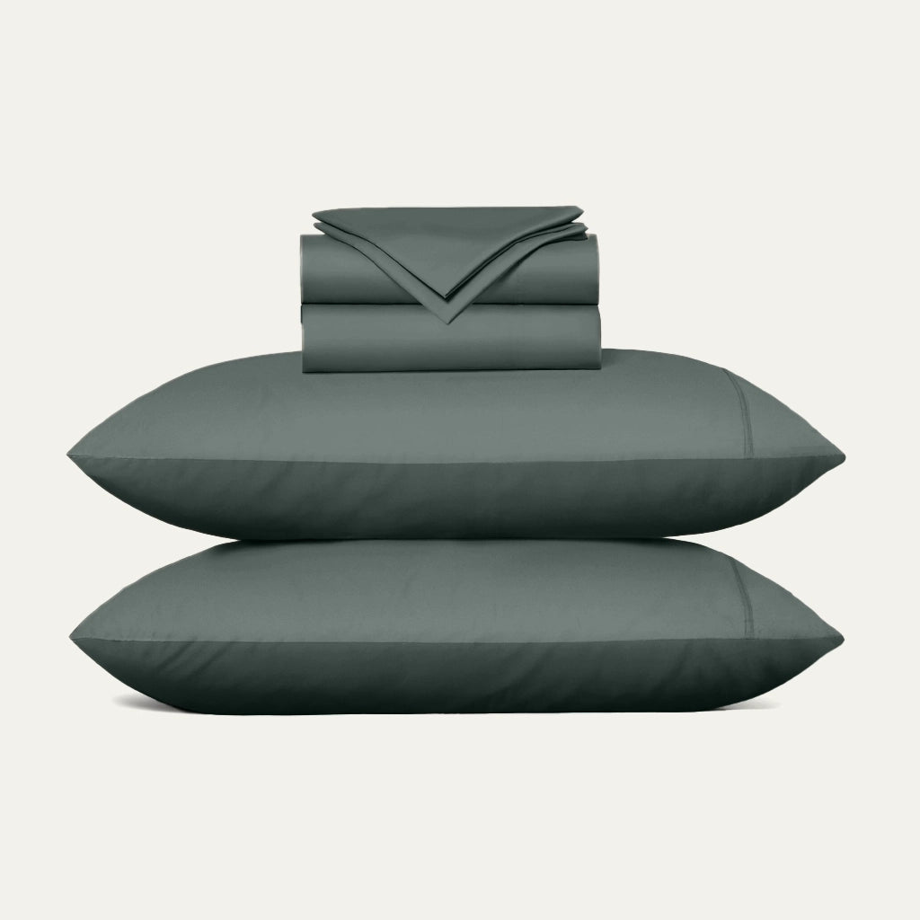 Set of green bedding including a duvet, two pillows, and a folded sheet on a light gray background.