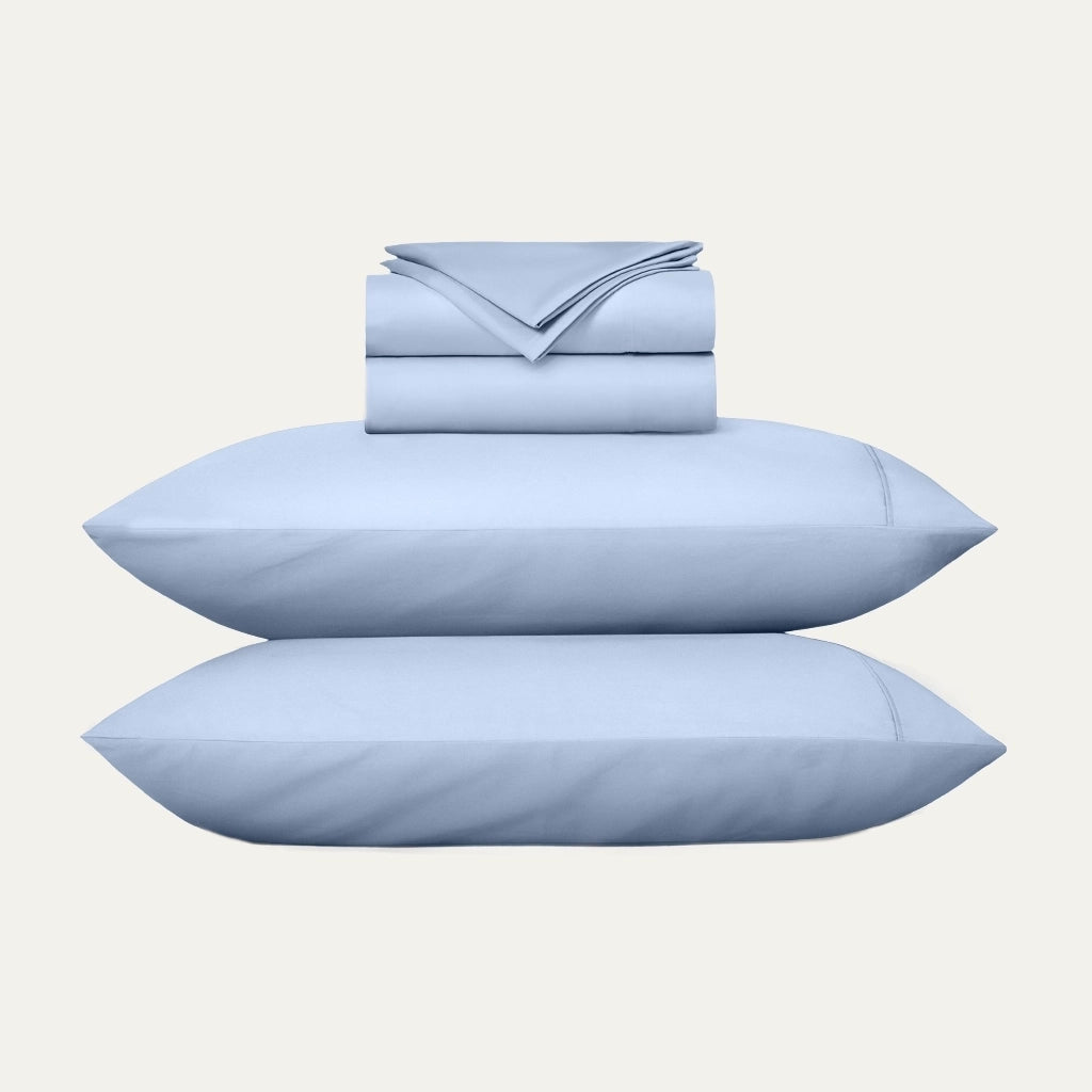 Set of light blue bedding including pillows and a folded sheet on a white background