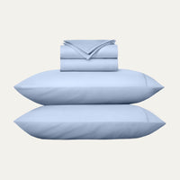 Set of light blue bedding including pillows and a folded sheet on a white background
