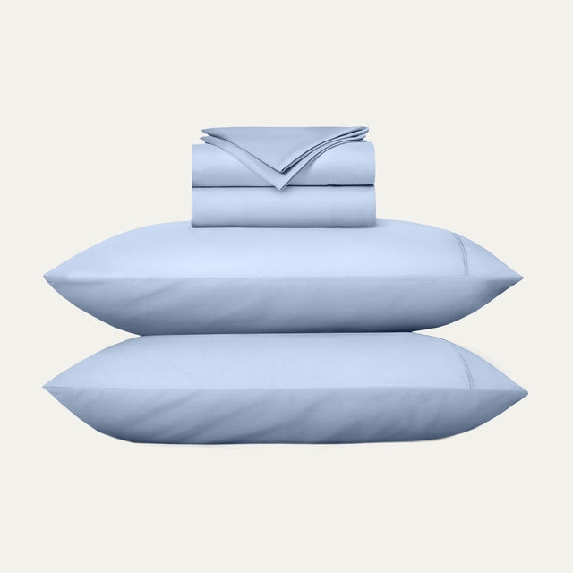 Set of light blue bedding including pillows and a folded sheet on a white background