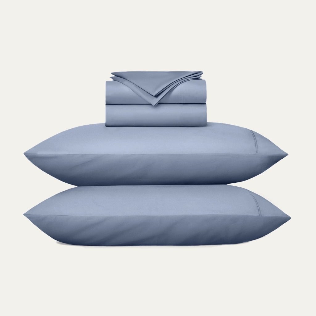 Blue bedding set with two pillows and a folded sheet on a white background