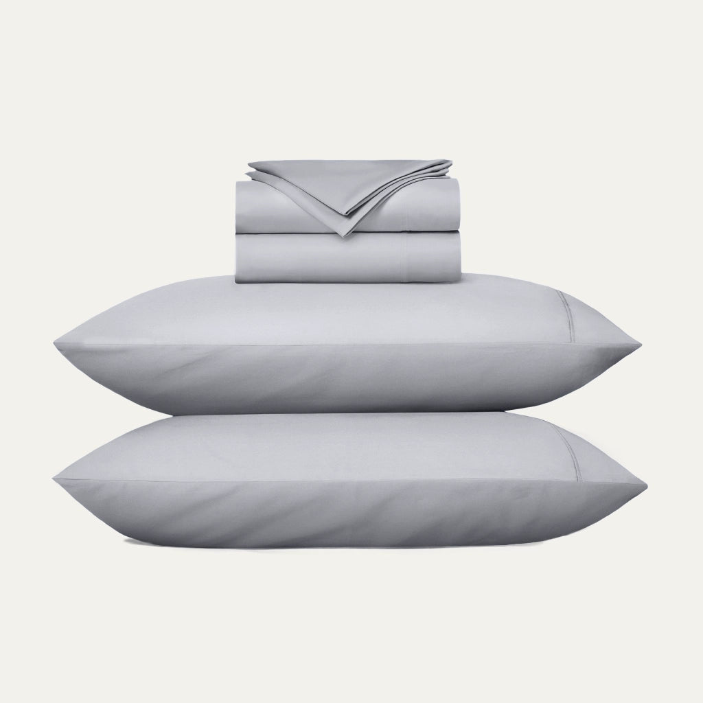 Gray bedding set with two pillows and a folded sheet on a white background