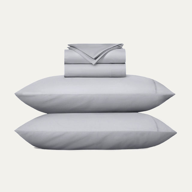 Gray bedding set with two pillows and a folded sheet on a white background