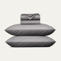 Gray bedding set including a duvet, two pillows, and a folded sheet on a white background