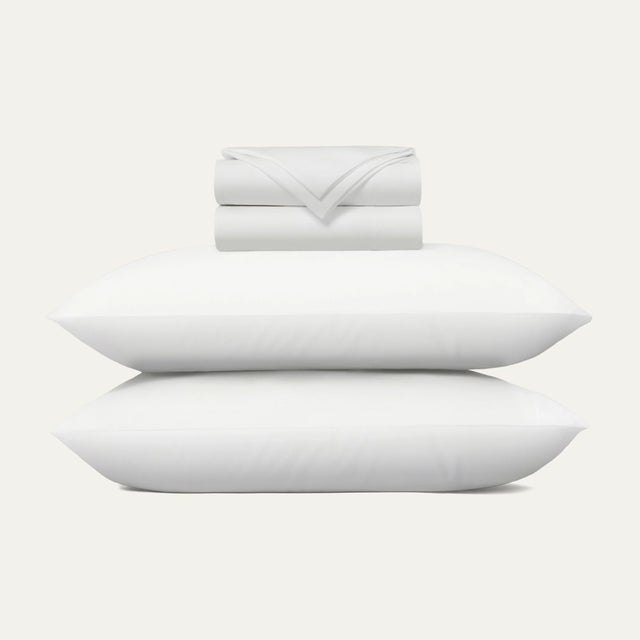 Set of white pillows and a folded blanket on a light gray background