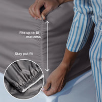 Person adjusting gray fitted sheet on a mattress with text indicating fit and stay put feature.