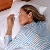Woman sleeping in bed with white pillows and a blue and white striped shirt.