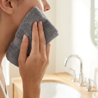 Person using a gray towel to wipe their face in a bathroom setting.
