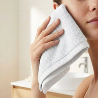 Person using a white towel to wipe their face in a bathroom setting