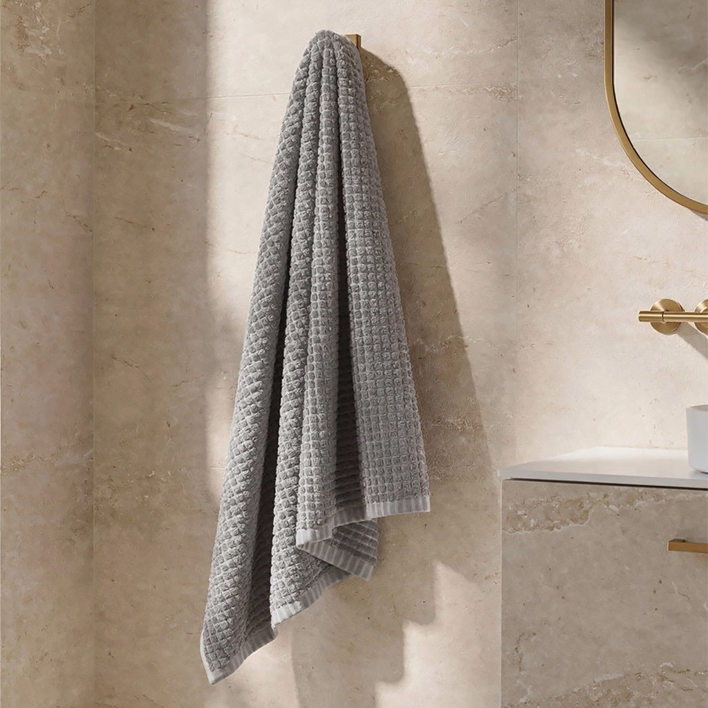 Gray textured towel hanging on a hook against a beige tiled wall.