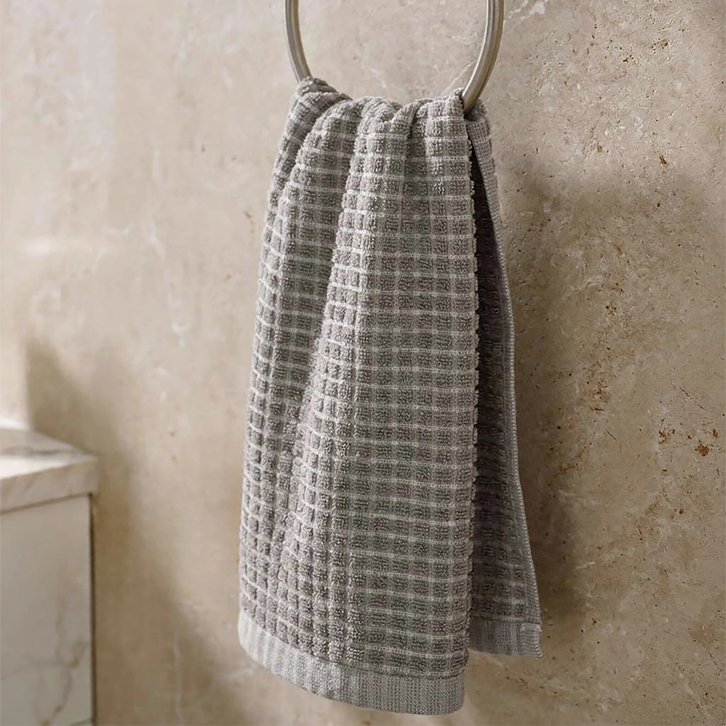 Textured gray towel hanging on a towel ring against a beige tiled wall.