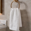 White textured towel hanging on a gold towel ring against a beige tiled wall.