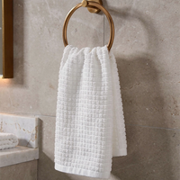 White textured towel hanging on a gold towel ring against a beige tiled wall.