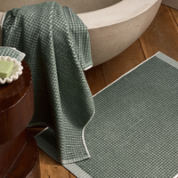 Green textured bath mat in front of a bathtub with a towel draped over the edge.