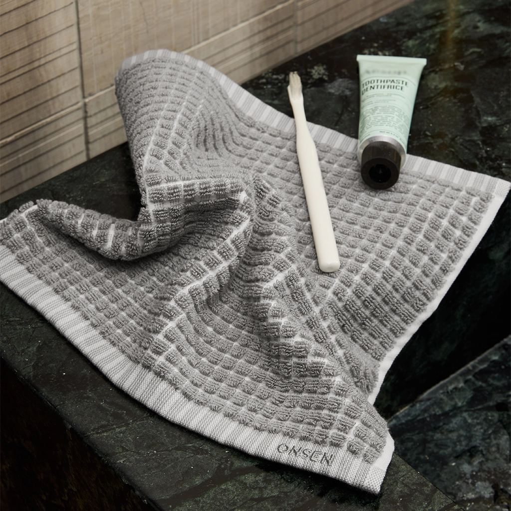 Gray textured towel on a dark surface with a tube of toothpaste and a toothbrush.