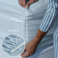 Person adjusting sky blue fitted sheet on a mattress with text indicating fit and stay put feature.